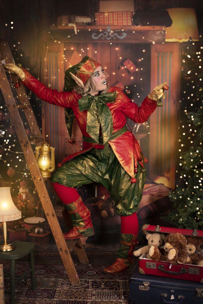 Cheeky Elf in enchanting Christmas attire, adorned with festive green and red colors, standing confidently on a ladder and playfully pointing with a finger. The delightful holiday decorations create a truly magical ambiance. The Elf's charming features include big ears and a cute bow, adding to the Christmas spirit. A perfect depiction of the joyous and Christmassy event atmosphere.