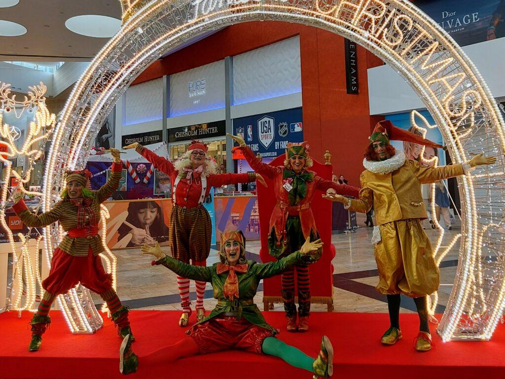 Enchanting group of elves posing for a photo at a Glasgow shopping center, immersed in festive Christmas decorations. Capturing the holiday spirit and magical ambiance.