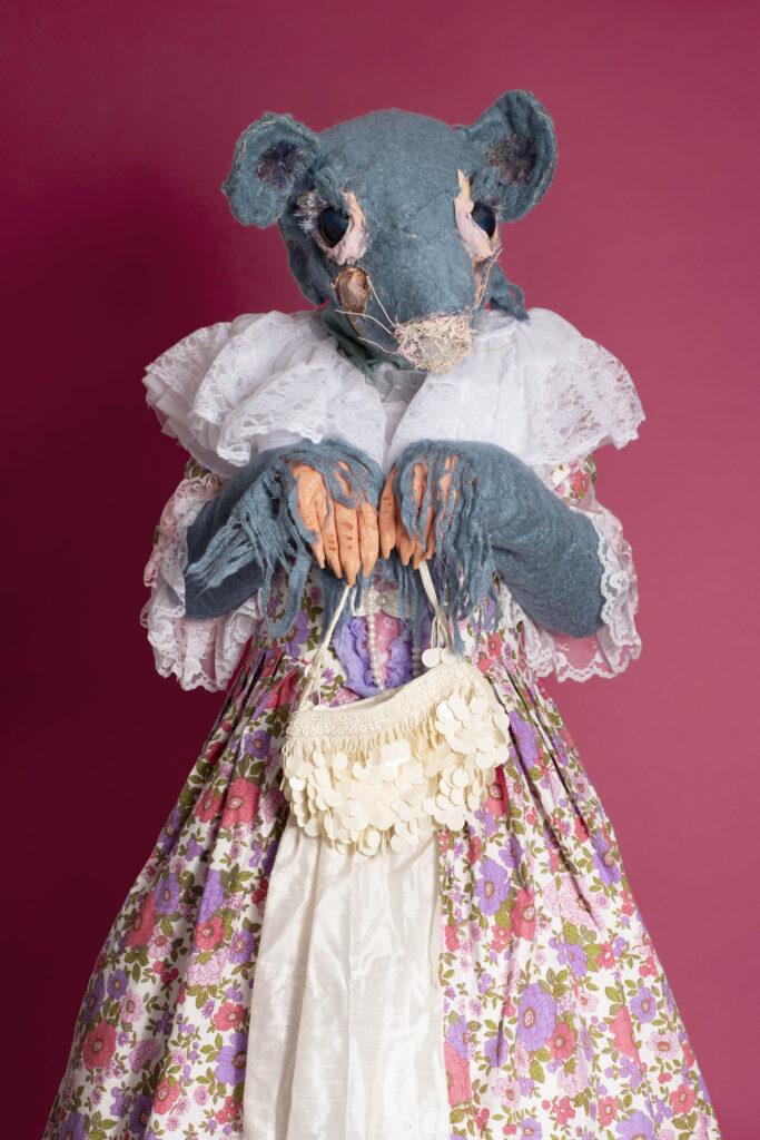  A fluffy blue mouse - character act-  in a Victorian dress adds whimsy, and the creamy bag suggests a touch of elegance. Against the pink background, the scene feels vibrant and inviting, perfect for a family-friendly event. The imagery evokes a sense of joy and wonder, making it an ideal choice for those interested in delightful animal acts.